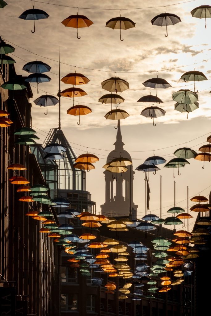 Regenschirme im Gegenlicht der tief stehenden Sonne über den Großen Bleichen, im Hintergrund ein Turm