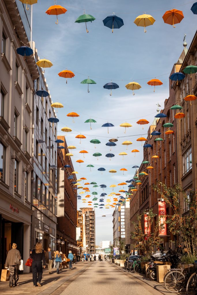 Orange, gelbe, grüne und blaue Regenschirme über der Straße im Passagenviertel bei blauem Himmel